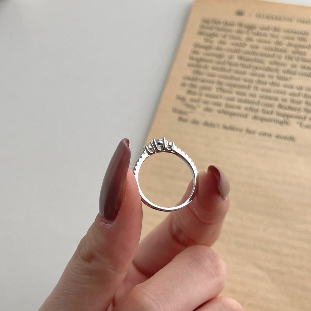 A dainty engagement ring featuring a central cubic zirconia stone with smaller stones on the band, set in a silver-tone mounting.