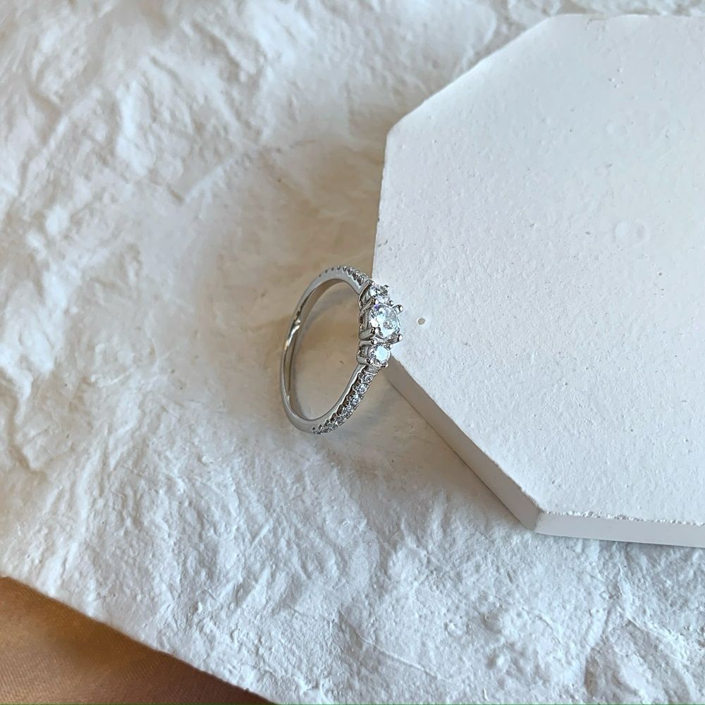A dainty engagement ring featuring a central cubic zirconia stone with smaller stones on the band, set in a silver-tone mounting.