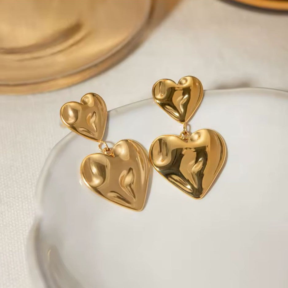 Gold heart-shaped earrings on a clear stand with a neutral background