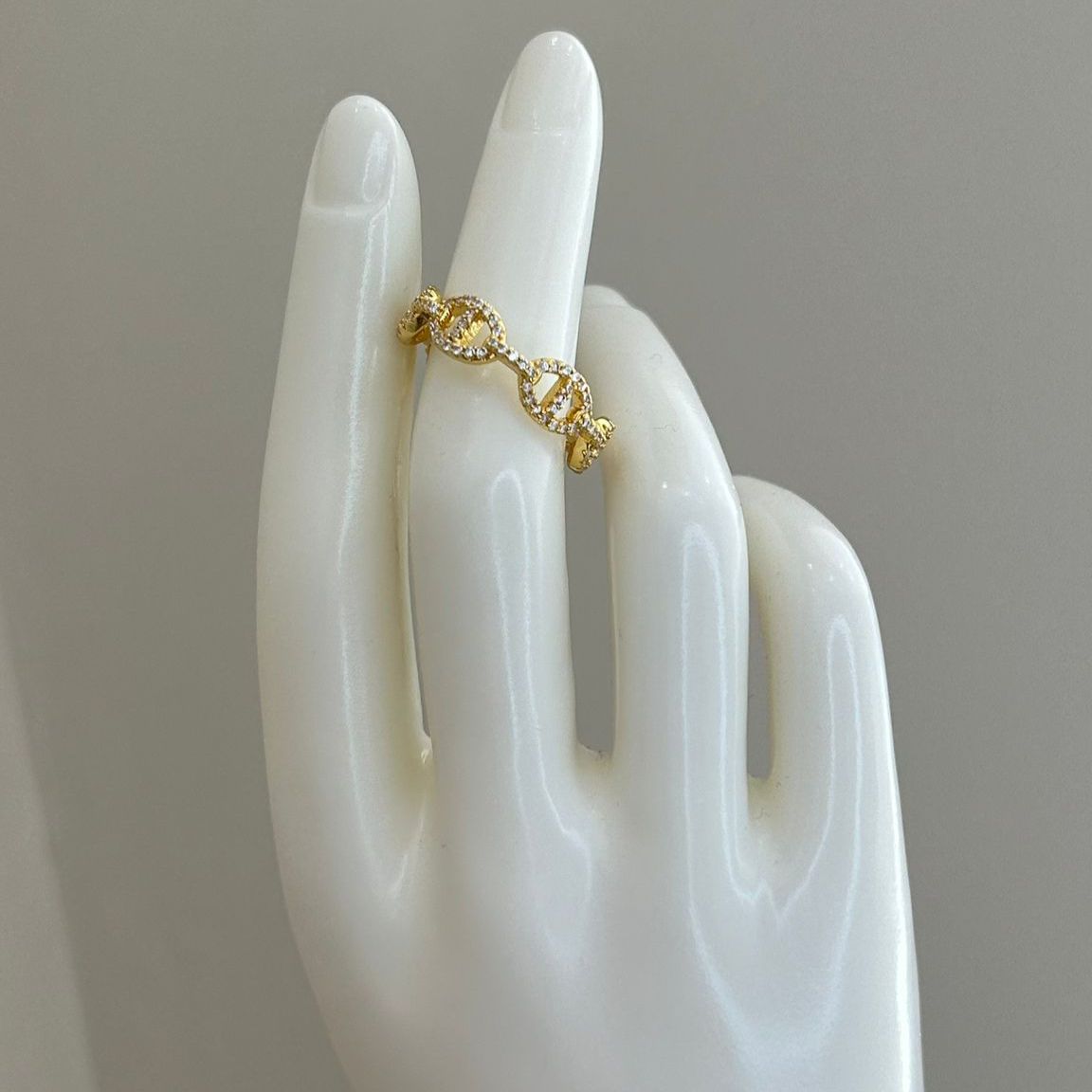 Gold ring on a white mannequin hand against a gray background
