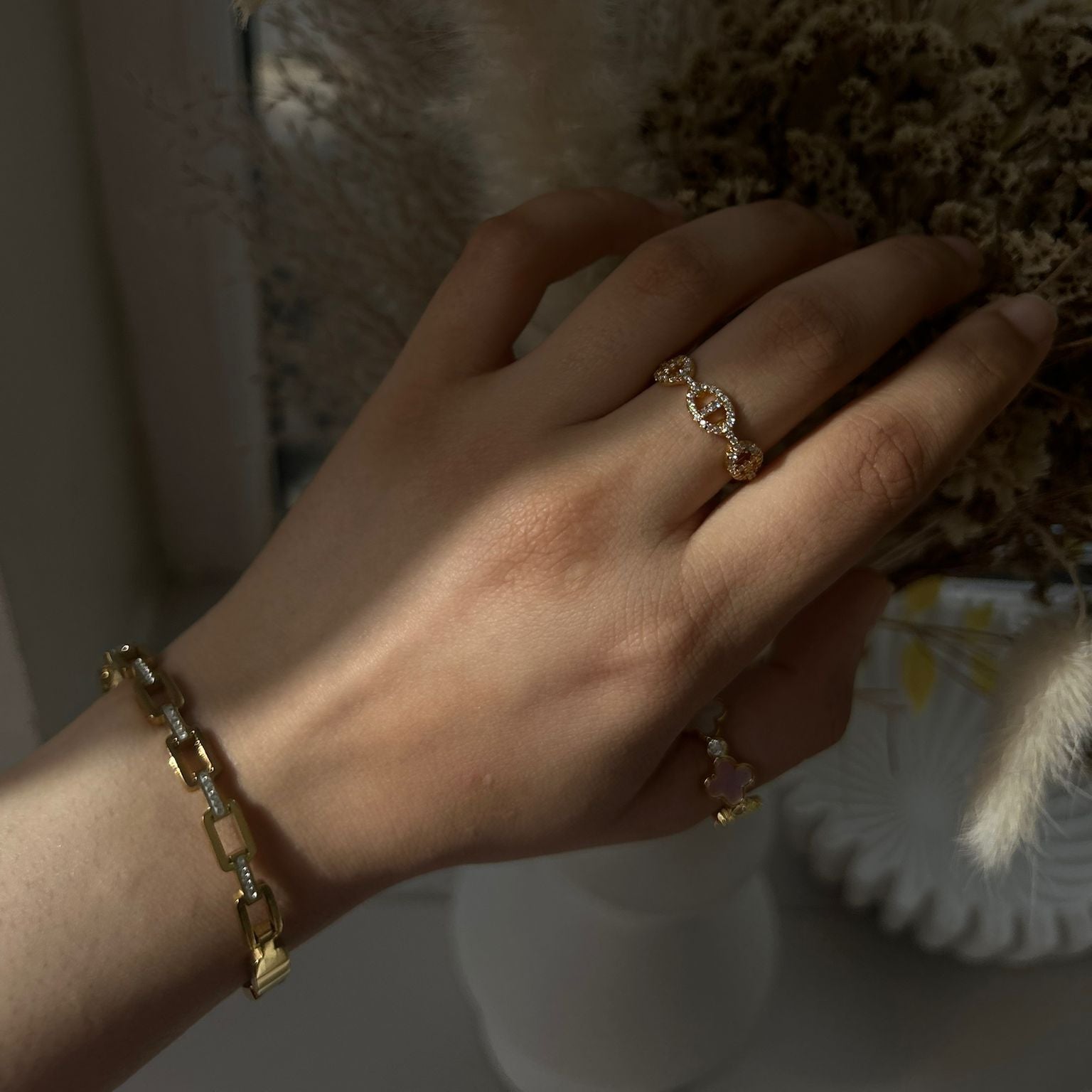 Hand wearing a gold ring and bracelet with a soft blurred background
