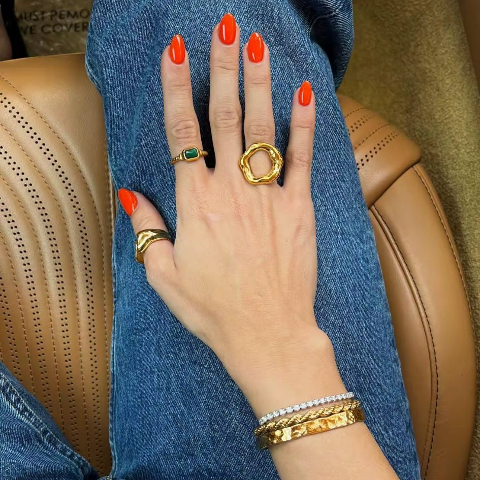 A gold metal hollow circle ring with an adjustable open design, displayed on a women's hand with blurred  background.