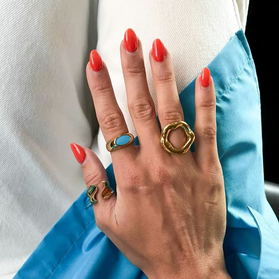 A gold metal hollow circle ring with an adjustable open design, displayed on a women's hand with blurred  background.