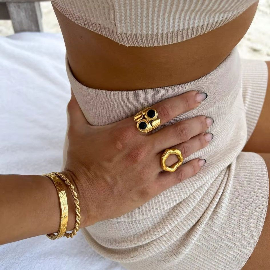 A gold metal hollow circle ring with an adjustable open design, displayed on a women's hand with blurred  background.