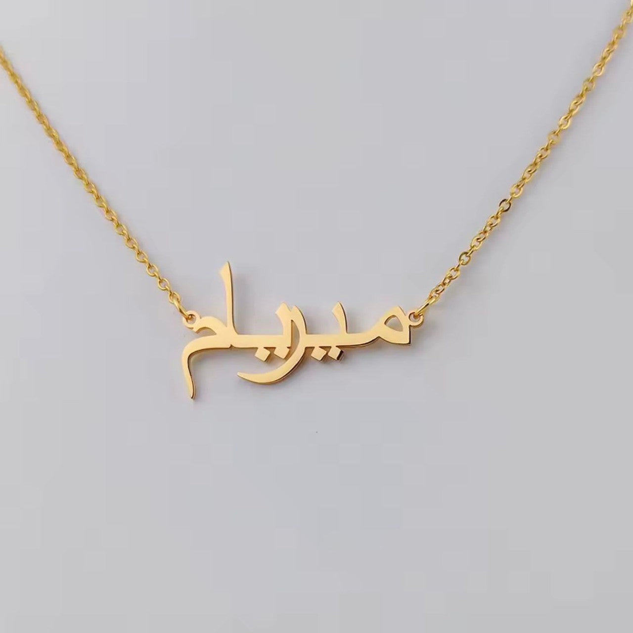 Gold necklace with Arabic name script on a gray background
