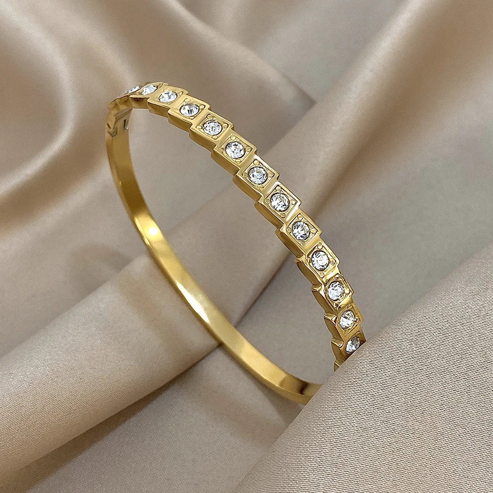 Gold bracelet with embedded crystals displayed on a beige fabric background