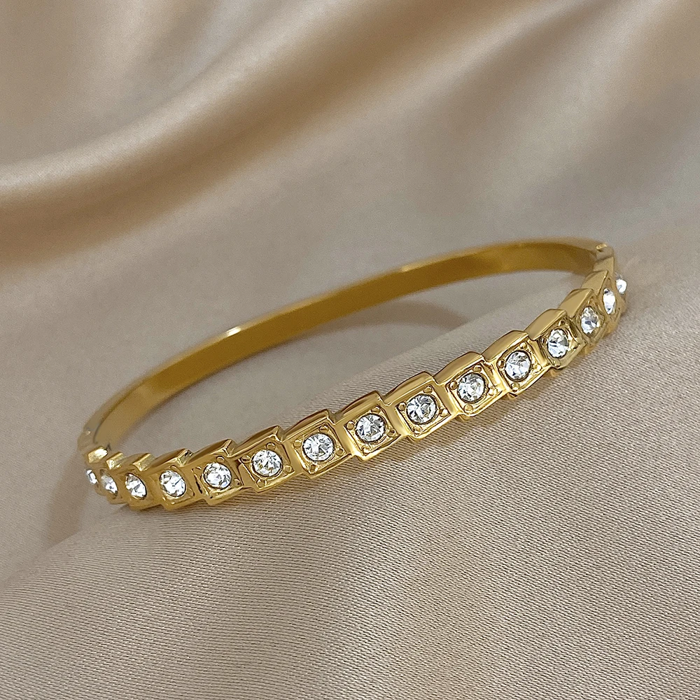 Gold bracelet with embedded crystals displayed on a beige fabric background