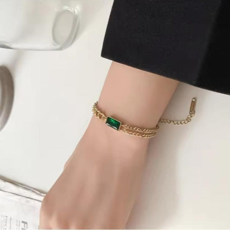 Gold bracelet with a green gemstone on a wrist against a white background