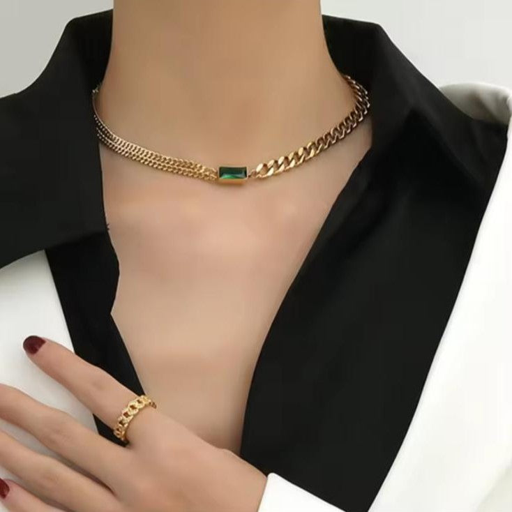 Gold ring and necklace chain with a green gemstone presented on a women against a blurred background