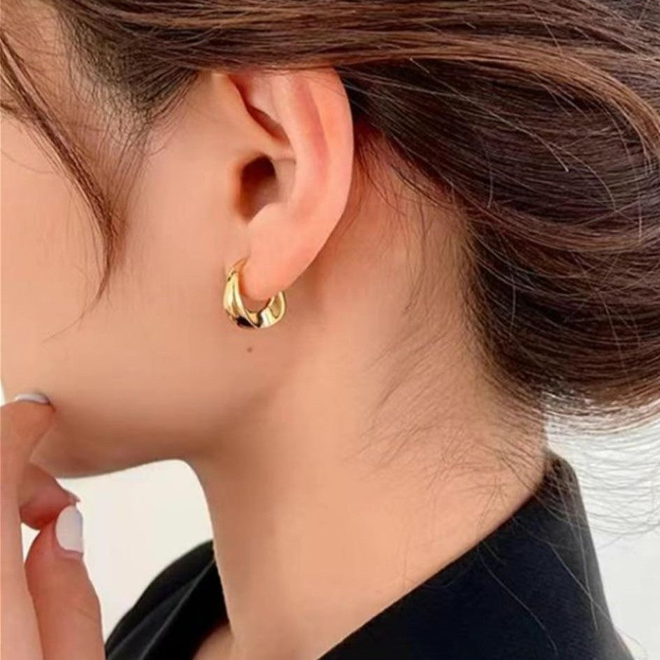A gold-colored hoop earring with a curved design, presented on a women's ear.