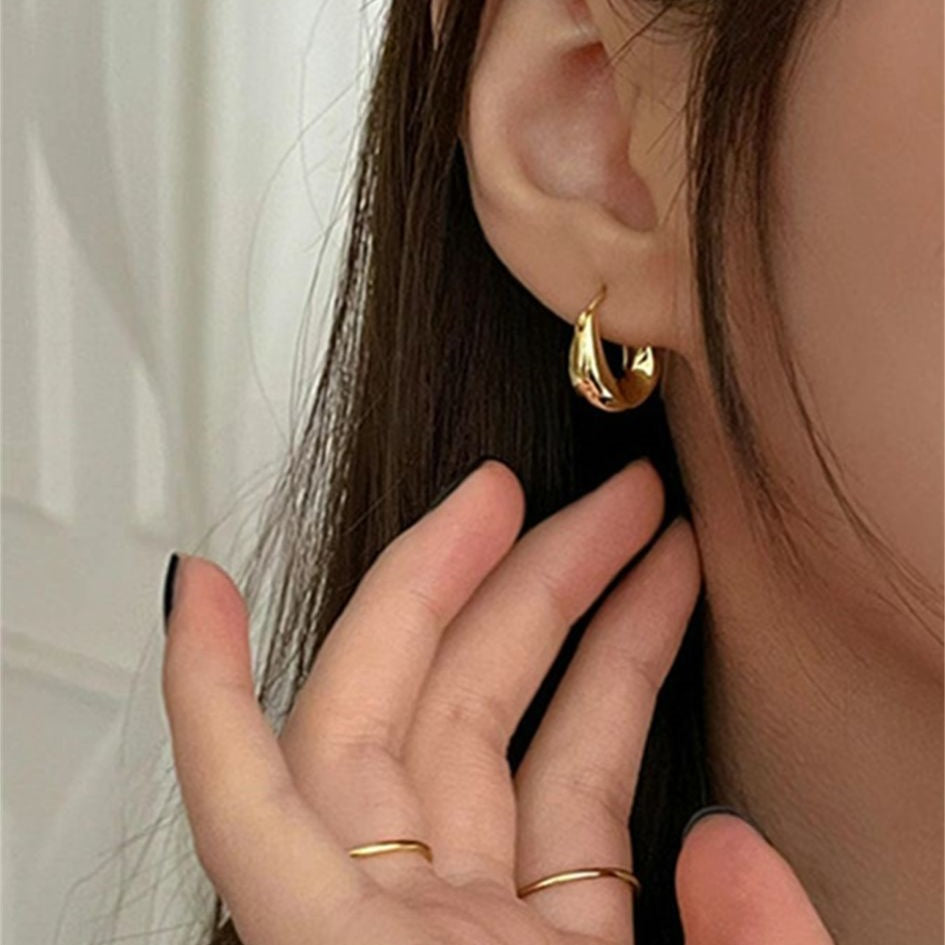 A gold-colored hoop earring with a curved design, presented on a women's ear.