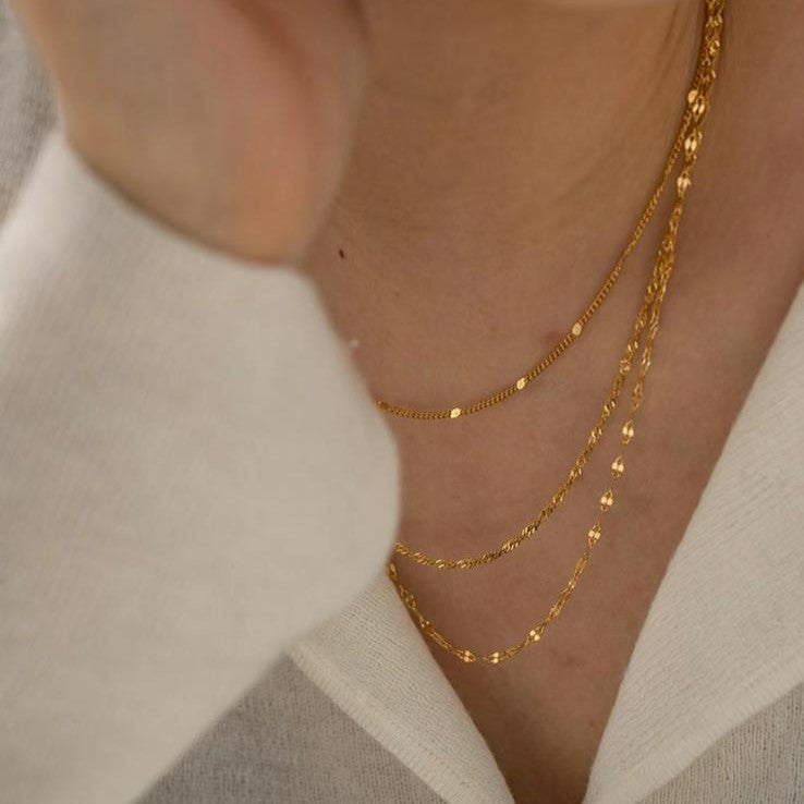 A gold-colored, layered chain necklace with three rows of stainless steel links.