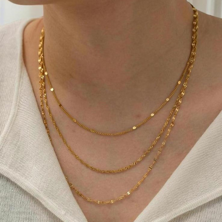 A gold-colored, layered chain necklace with three rows of stainless steel links.