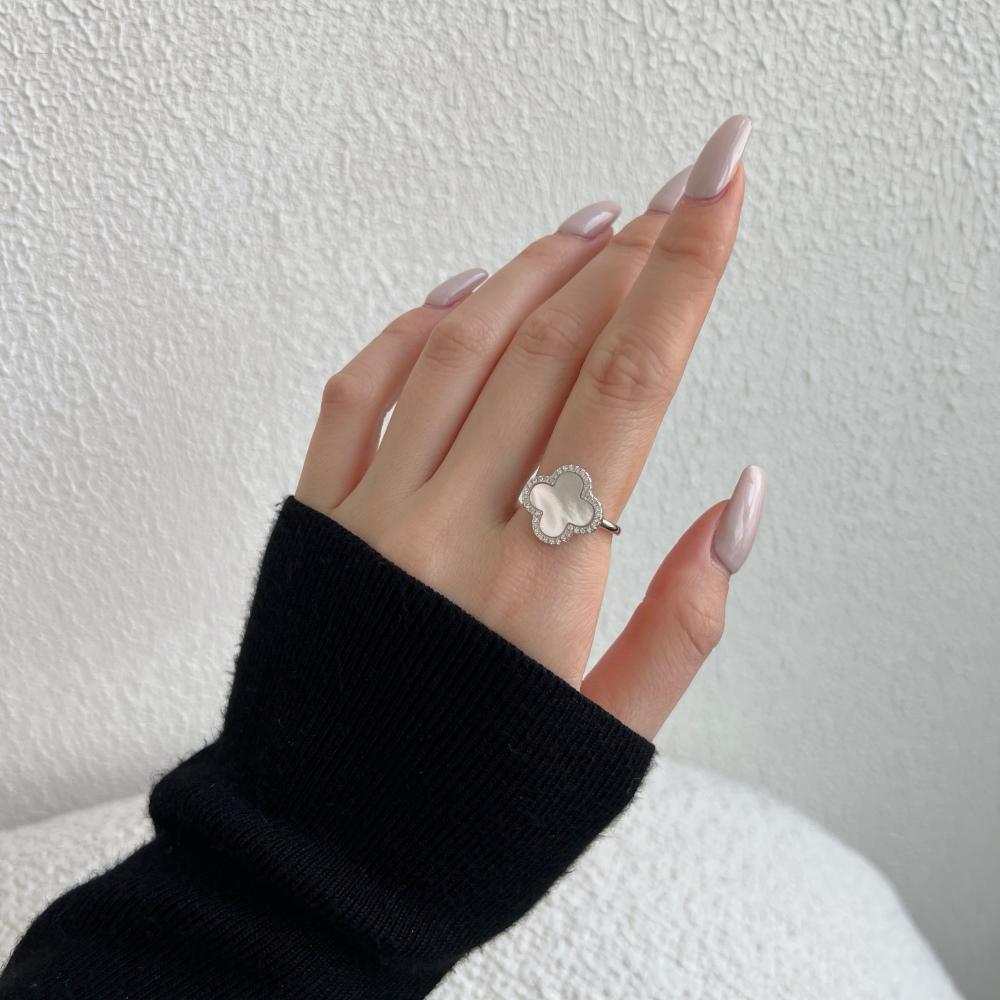 A clover-shaped ring with white shell accents, in 925 sterling silver with a rhodium plating, displayed against a white background on a women's hand.
