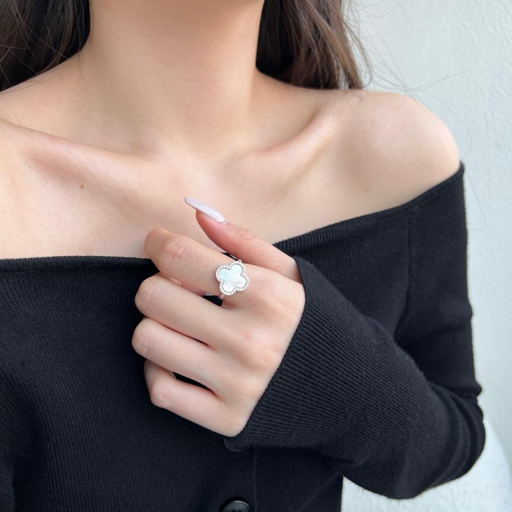 A clover-shaped ring with white shell accents, in 925 sterling silver with a rhodium plating, displayed against a white background on a women's hand.