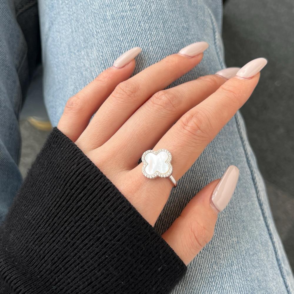 A clover-shaped ring with white shell accents, in 925 sterling silver with a rhodium plating, displayed on a women's hand.