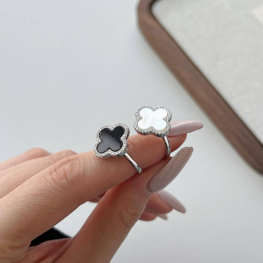 A pair of clover-shaped rings with black and white shell accents, in 925 sterling silver with a rhodium plating, displayed against a white background.