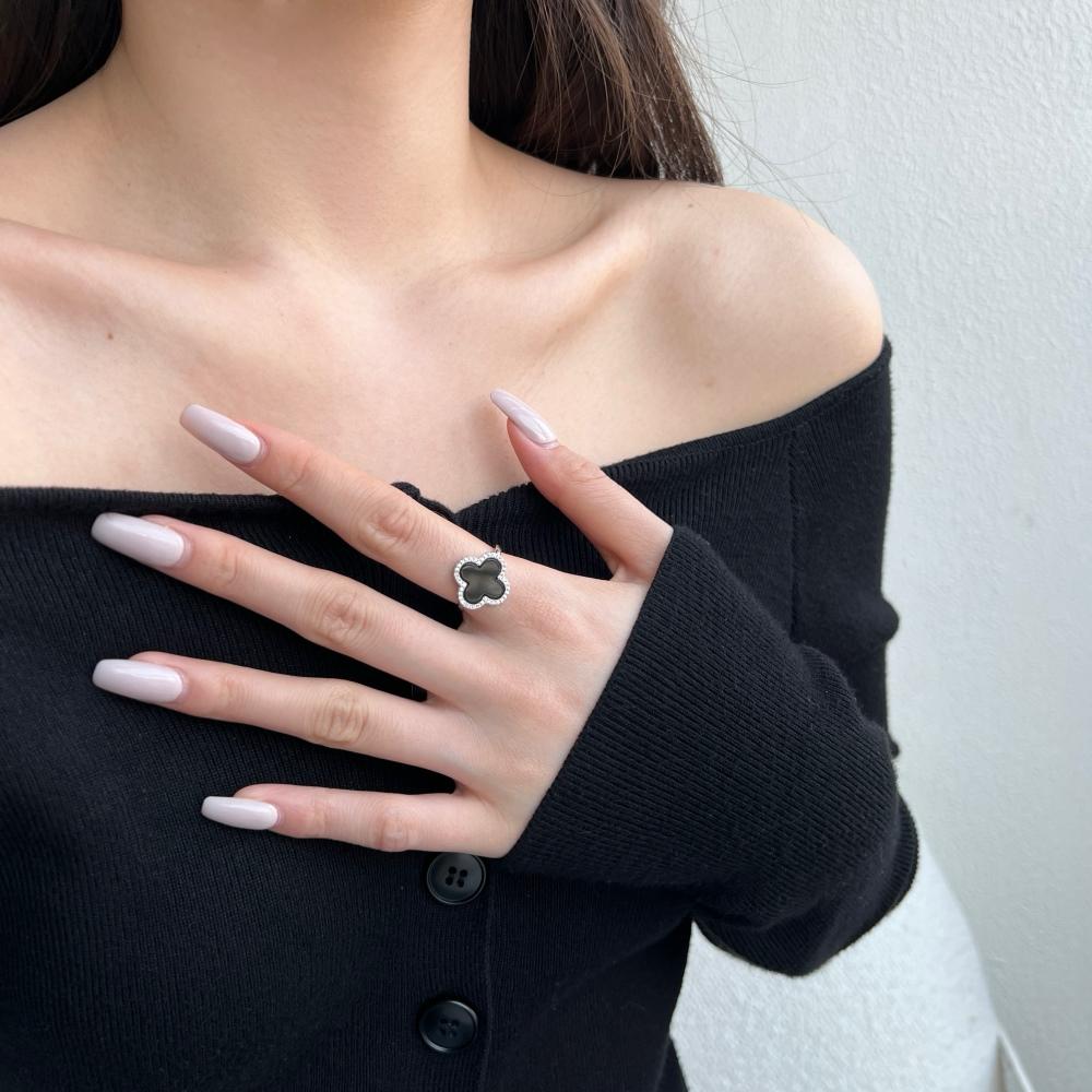 A clover-shaped ring with black shell accent, in 925 sterling silver with a rhodium plating, displayed against a white background on a woman's hand.