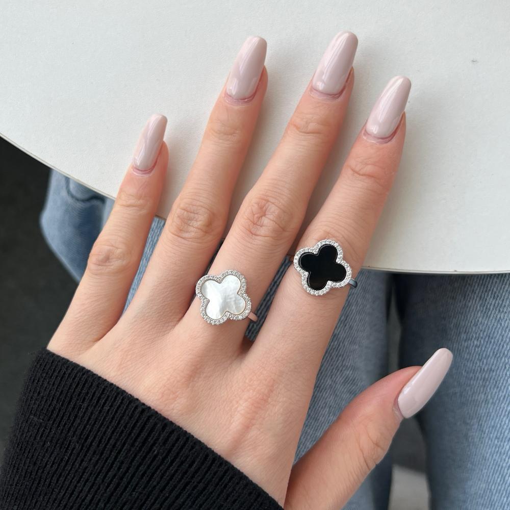 A pair of clover-shaped rings with black and white shell accents, in 925 sterling silver with a rhodium plating, displayed against a white background on a women's hand.