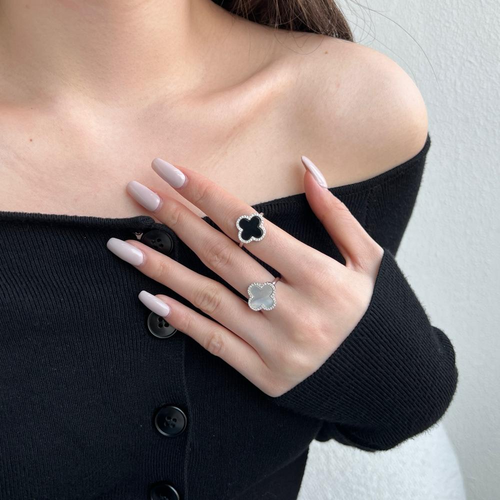 A pair of clover-shaped rings with black and white shell accents, in 925 sterling silver with a rhodium plating, displayed against a white background on a women's hand.