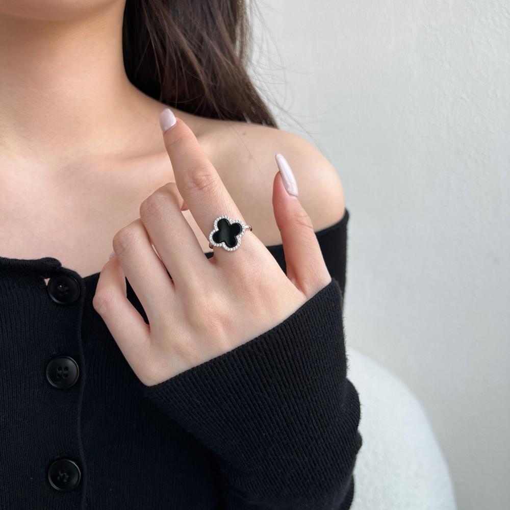 A clover-shaped ring with black shell accents, in 925 sterling silver with a rhodium plating, displayed against a white background on a women's hand.