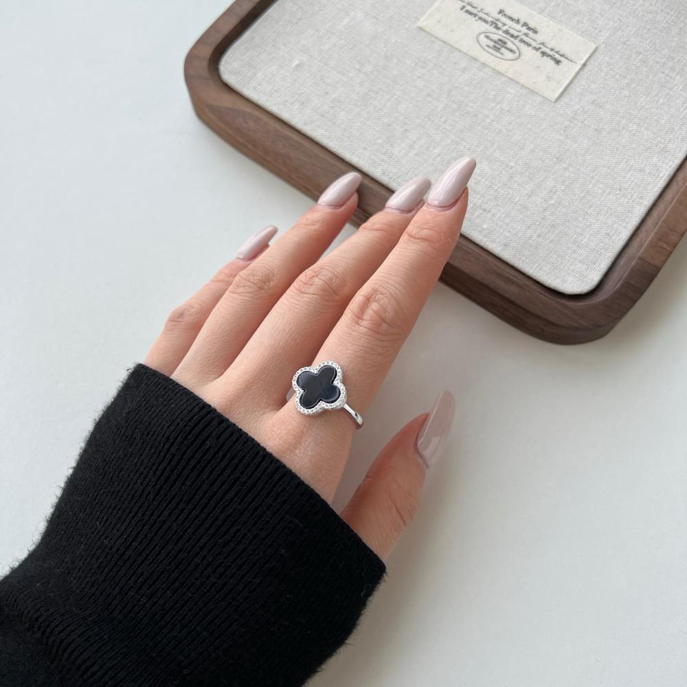 A clover-shaped ring with black shell accent, in 925 sterling silver with a rhodium plating, displayed against a white background on a women's hand.