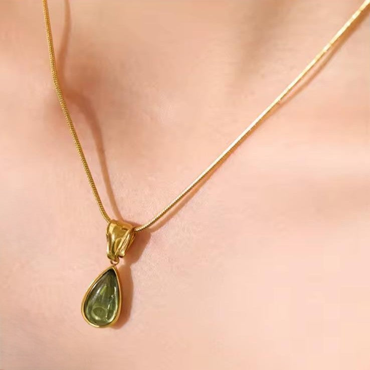 Gold necklace with a green teardrop pendant on a women's neck.