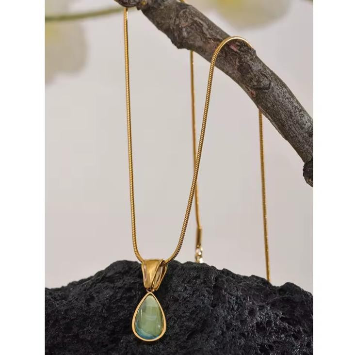 Gold necklace with a green teardrop pendant on a branch
