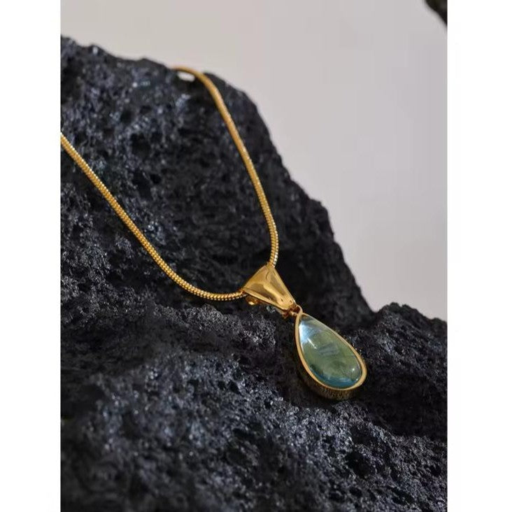 Gold necklace with a green teardrop pendant on a rock