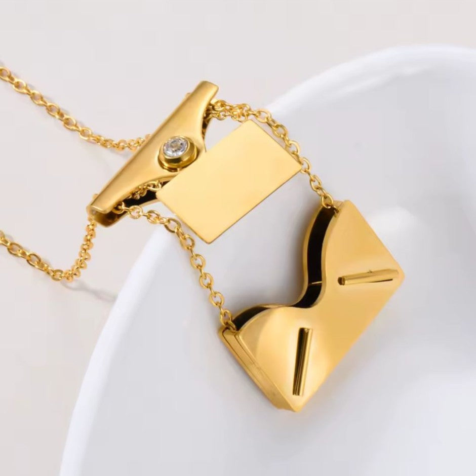 Gold necklace with a envelope pendant on a white dish