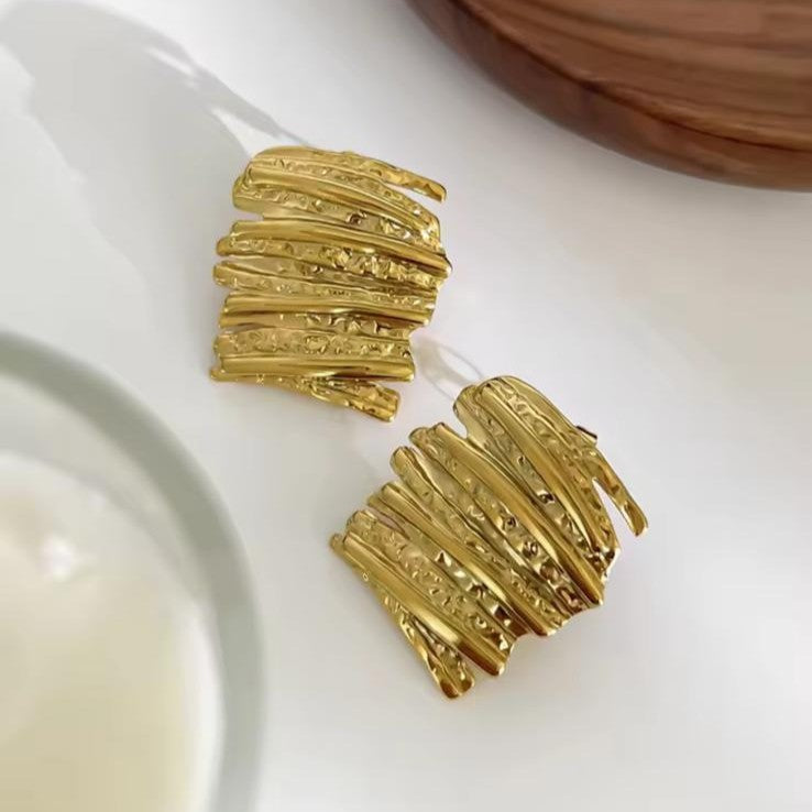 Gold textured abstract earrings on a white surface