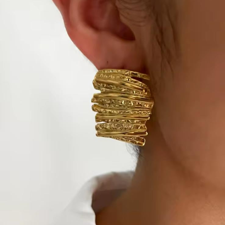 Abstract Gold textured earrings worn by a person on a white background
