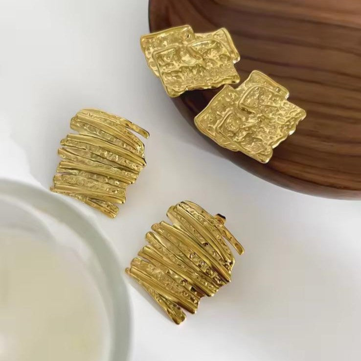Gold textured abstract earrings on a white and brown surface