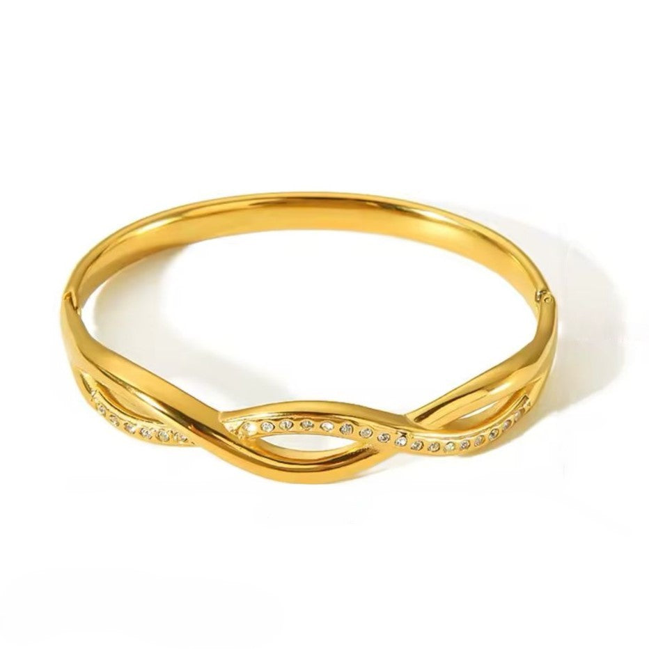 A gold-colored stainless steel bangle bracelet with an infinity symbol design, featuring sparkling accents on the loops.