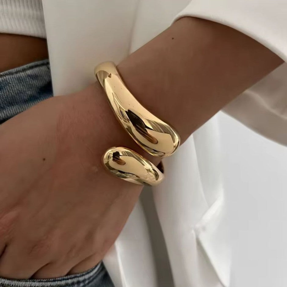 Gold bangle on a wrist with a neutral background