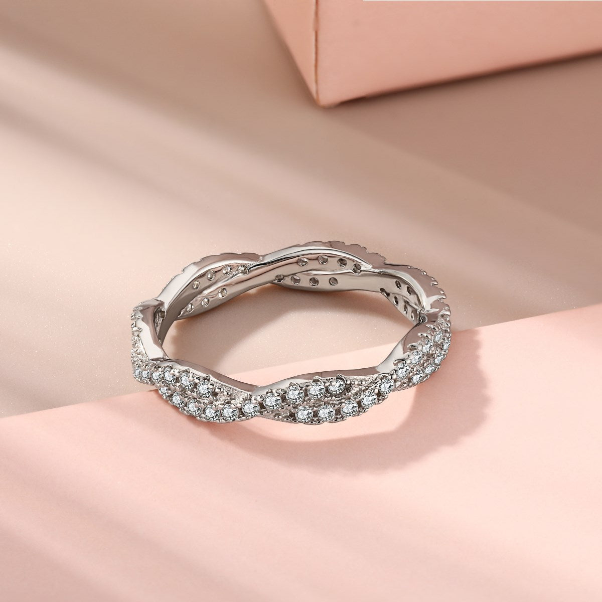 A sterling silver twist ring with multiple pave-set crystals adorning its surface on a pink background.