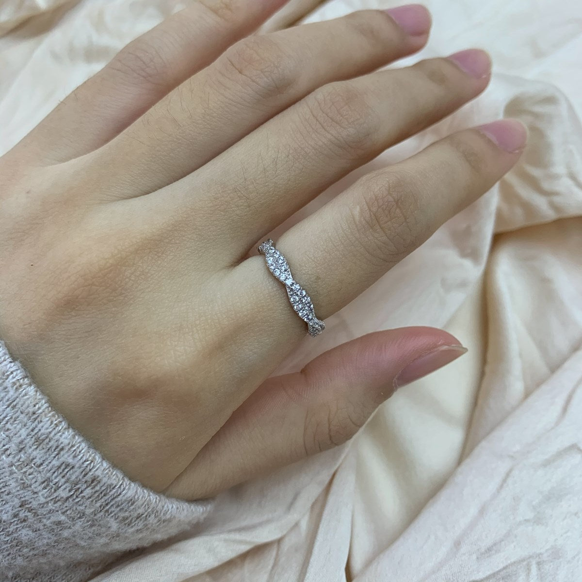 A sterling silver twist ring with multiple pave-set crystals adorning its surface on a white fabric in the background.