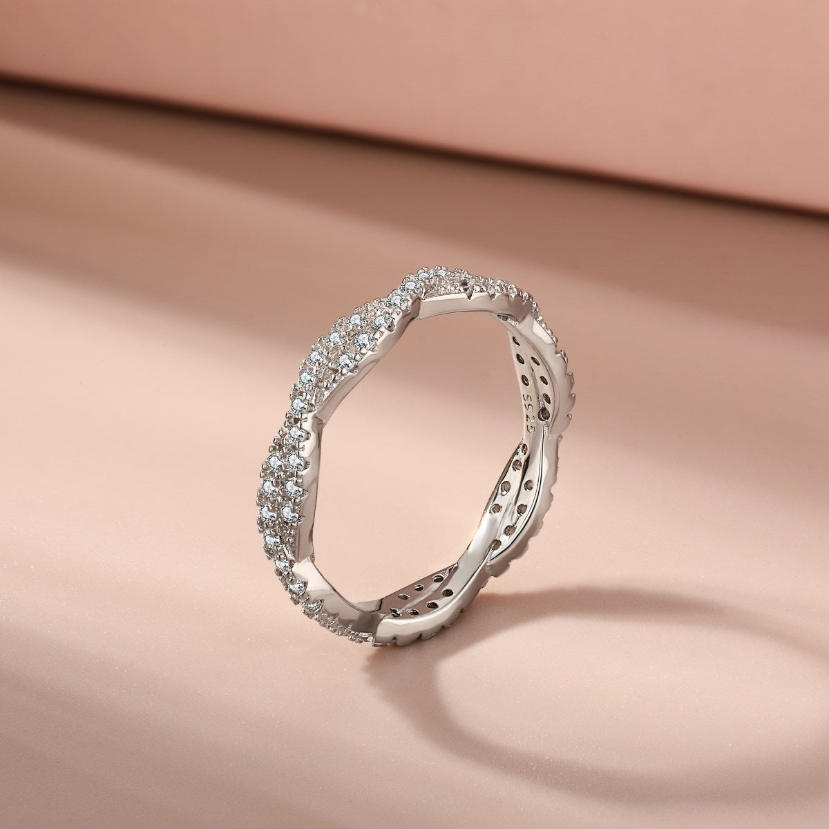 A sterling silver twist ring with multiple pave-set crystals adorning its surface on a pink background.