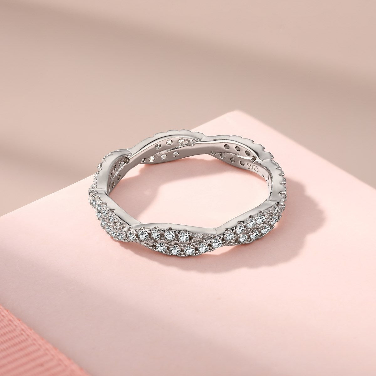 A sterling silver twist ring with multiple pave-set crystals adorning its surface on a pink background.