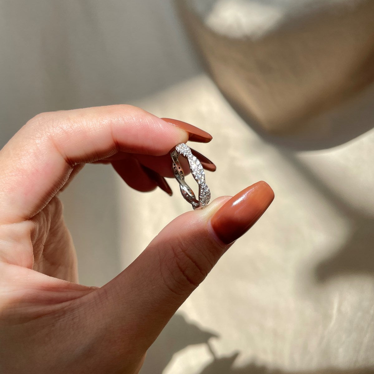 A sterling silver twist ring with multiple pave-set crystals adorning its surface in a hand with blurred background.