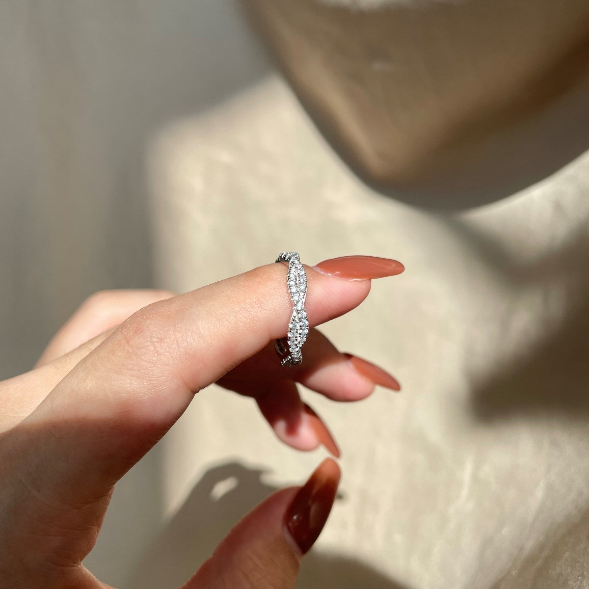 A sterling silver twist ring with multiple pave-set crystals adorning its surface in a hand with blurred background.