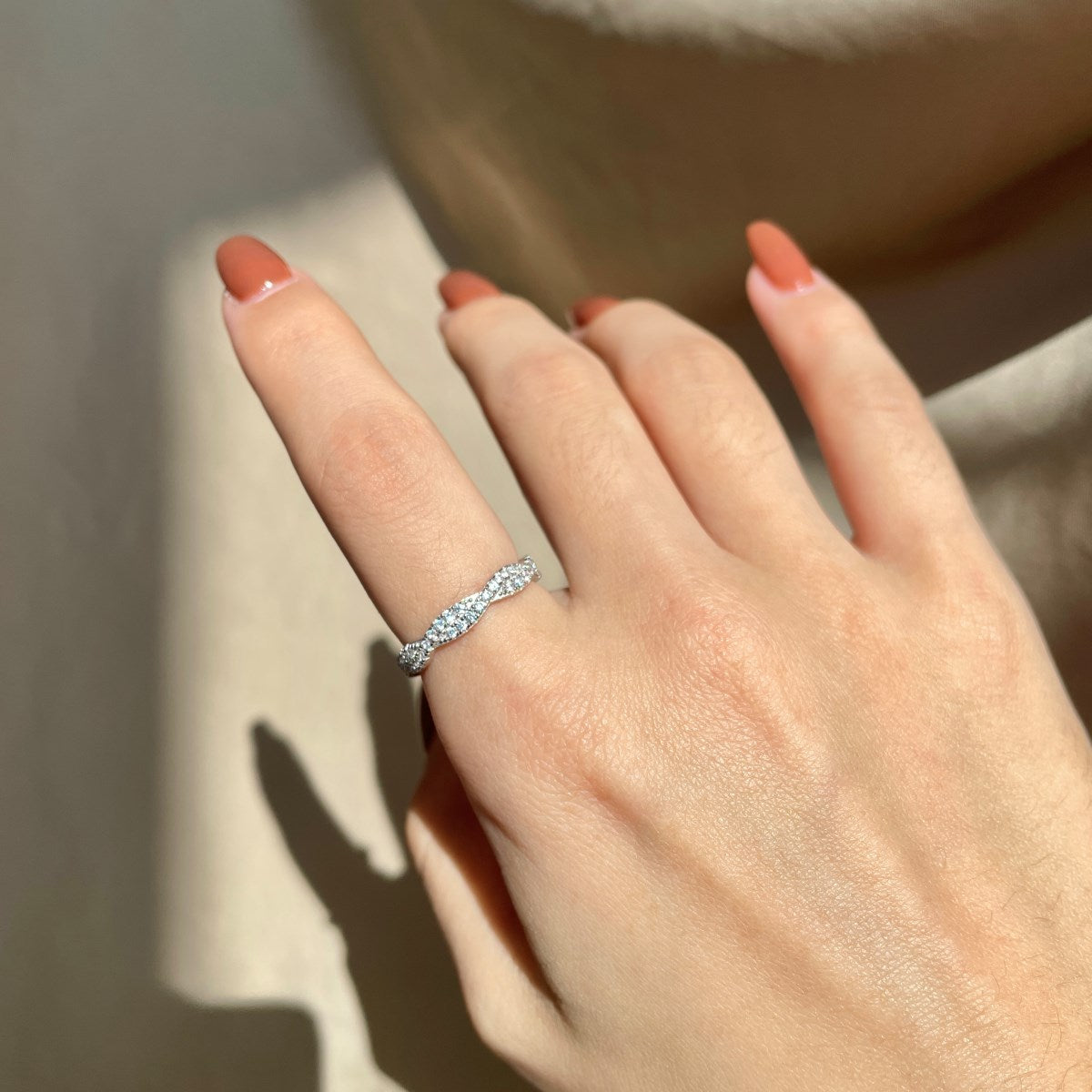 A sterling silver twist ring with multiple pave-set crystals adorning its surface in a hand with blurred background.