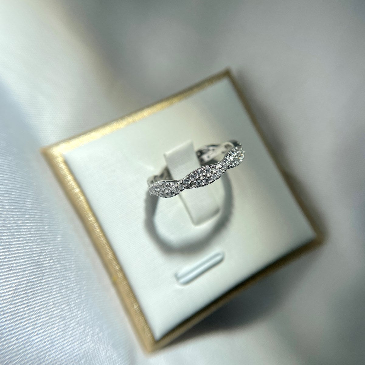 A sterling silver twist ring with multiple pave-set crystals adorning its surface with blurred background.
