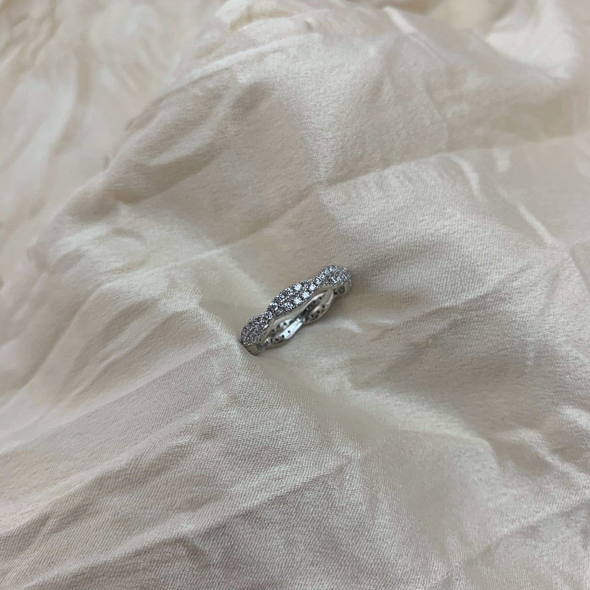 A sterling silver twist ring with multiple pave-set crystals adorning its surface on a white fabric in the background.