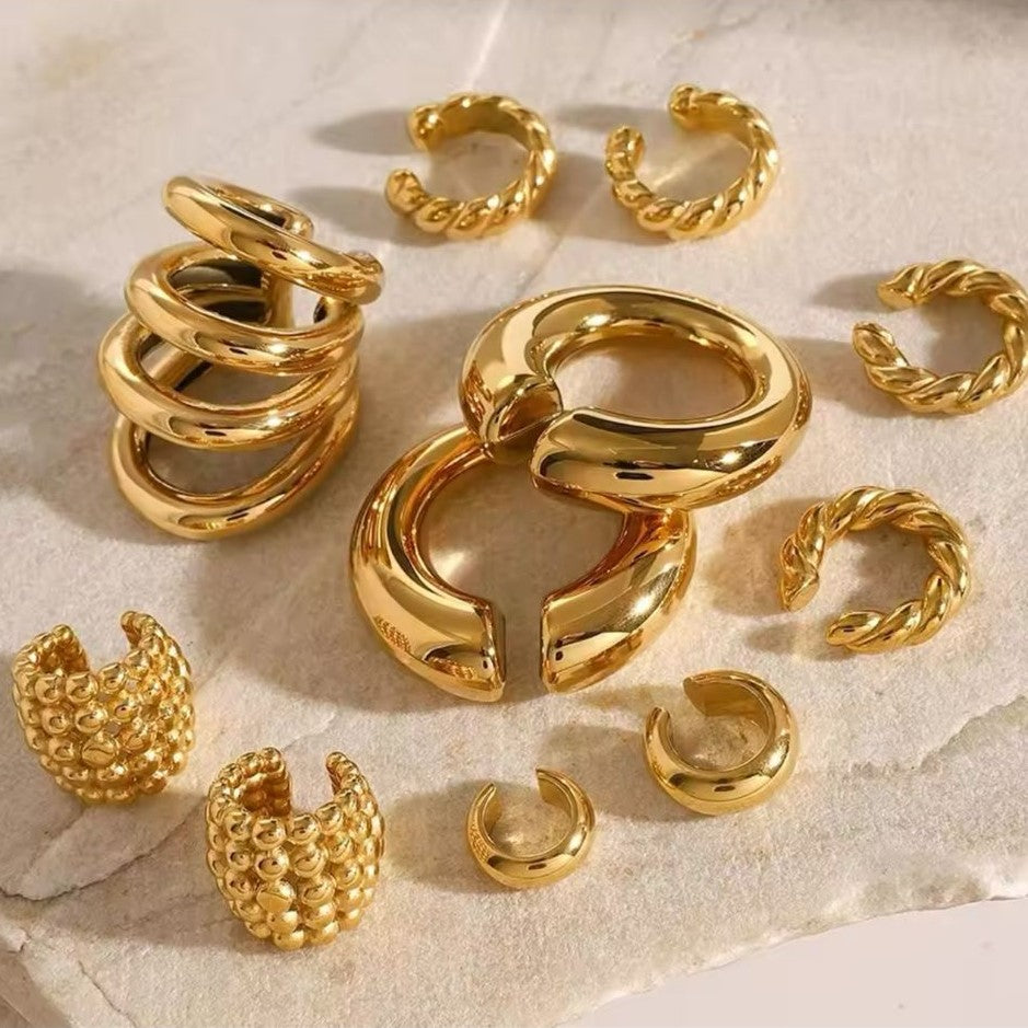 A collection of gold-colored ear cuffs with varying designs displayed on a neutral background.