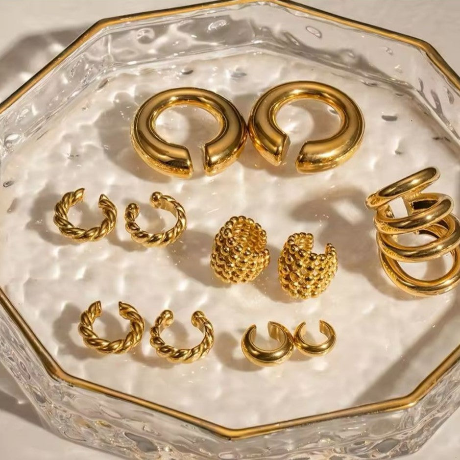 A collection of gold-colored ear cuffs with different luxury designs displayed on a tray.