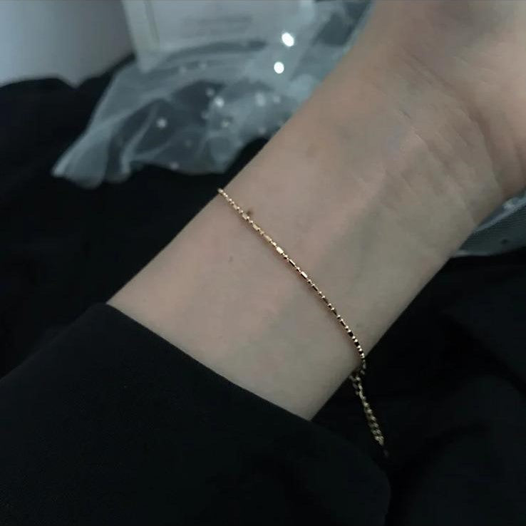 A sterling silver whisper chain bracelet displayed on a wrist against a dark background.