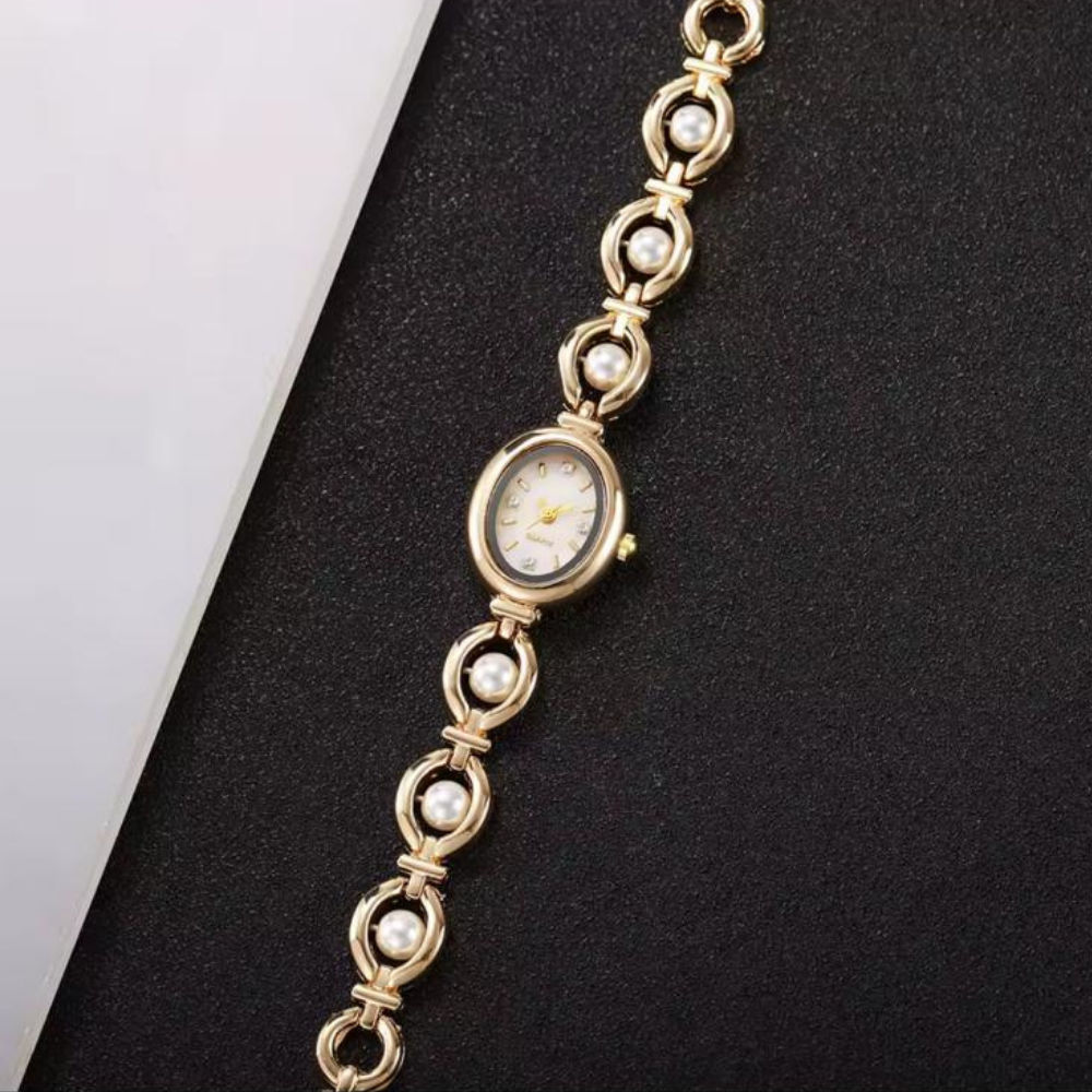 Gold bracelet watch with pearl accents on a black surface