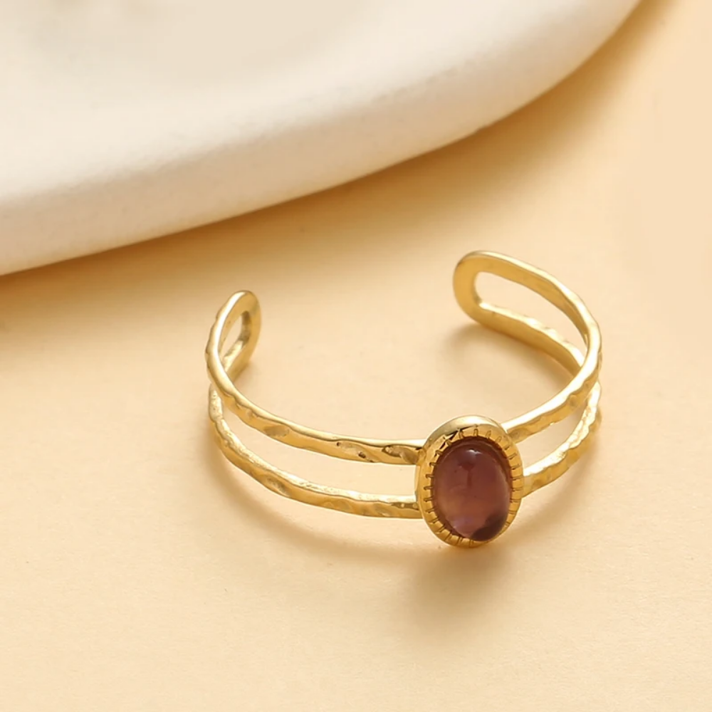 Gold ring with a red gemstone on a beige background