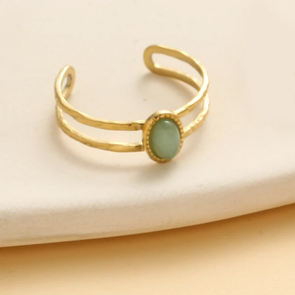 Gold ring with a green stone on a beige background